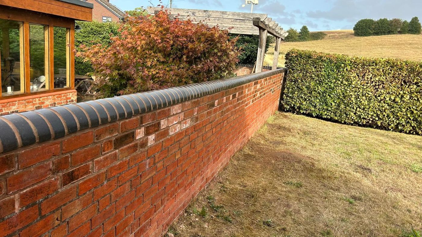 Red brick wall with black bullnose coping running along a garden lawn