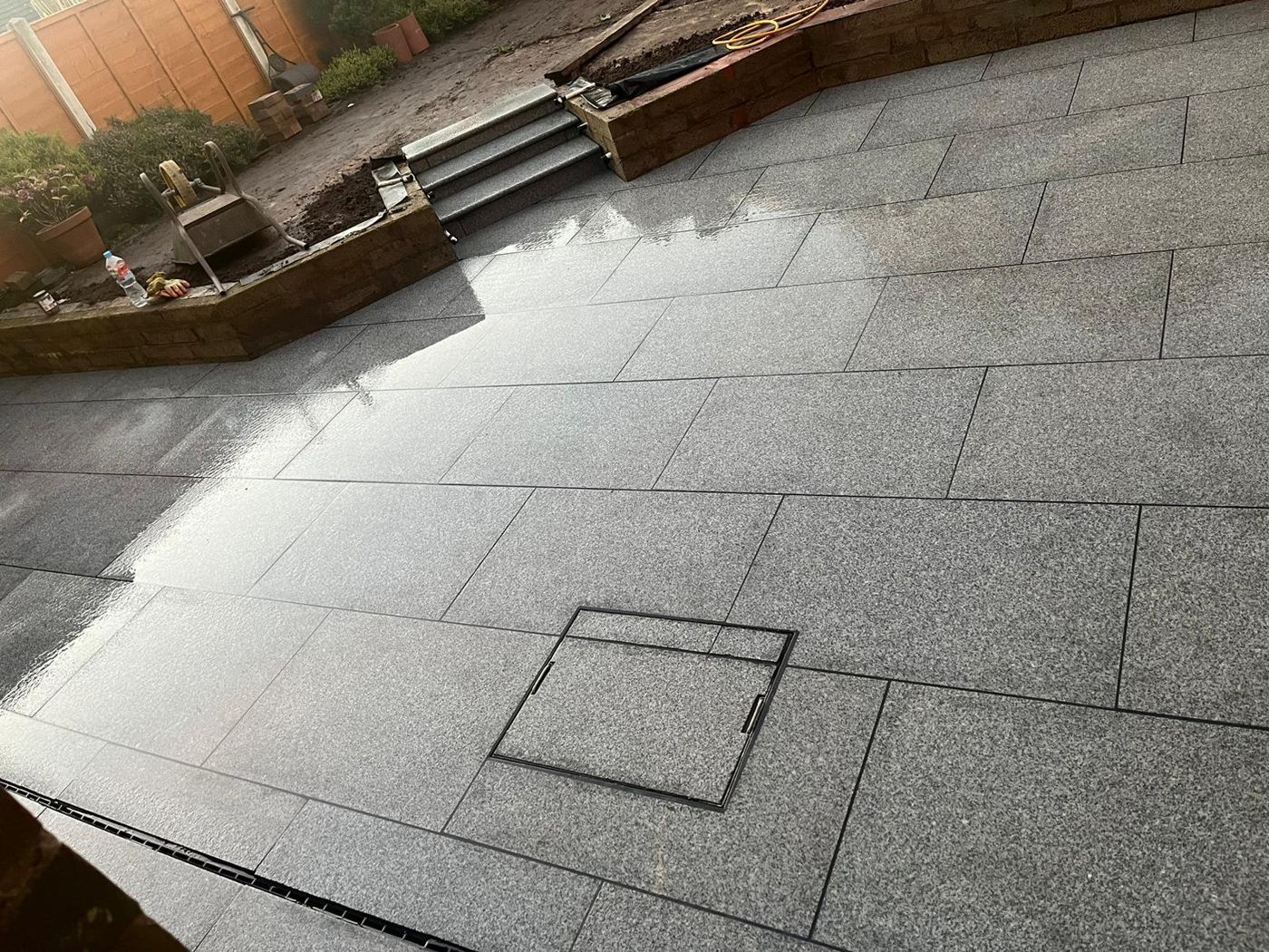 Large-format grey granite patio with stone steps and a channel drain
