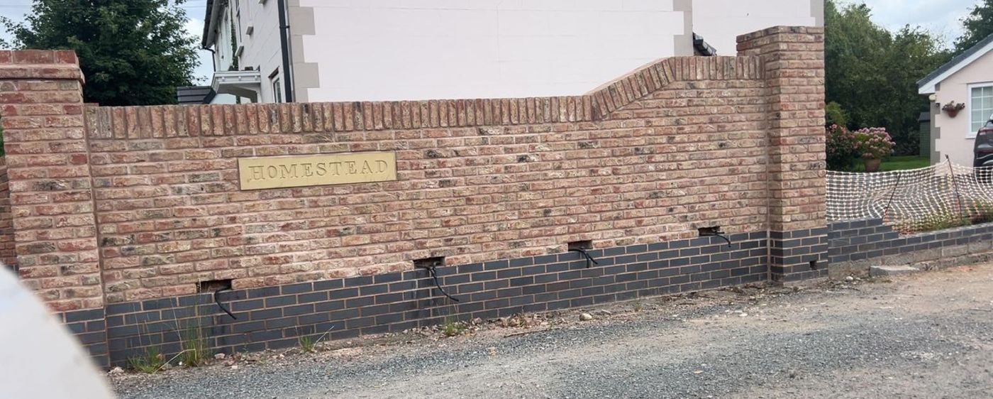 Curved-top reclaimed brick wall on a blue brick plinth with a brass name plaque