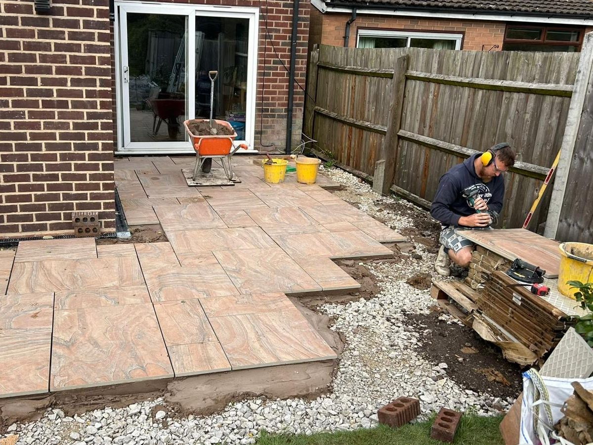 Porcelain patio slabs being laid on a mortar bed behind a brick house