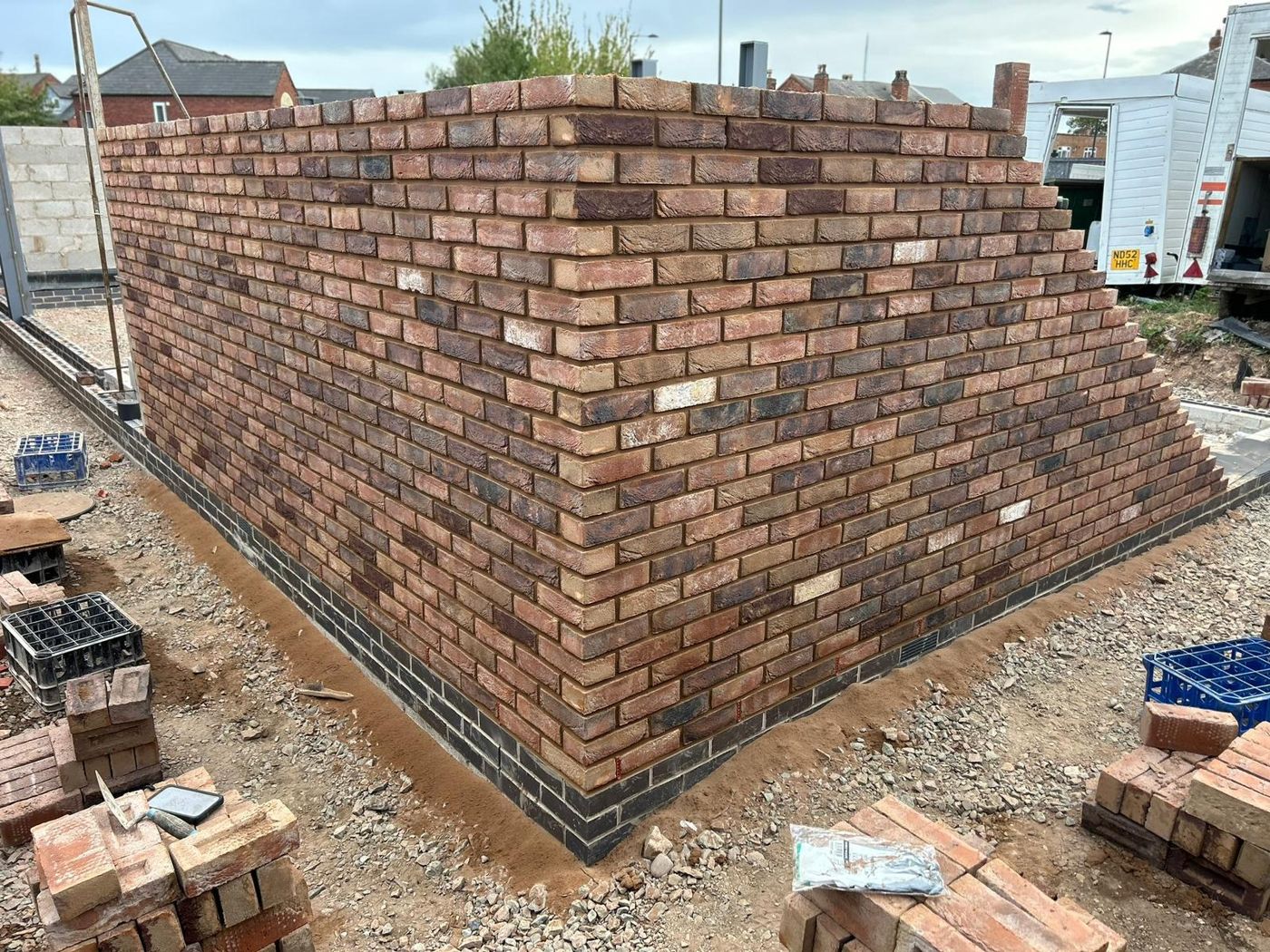Corner of a new facing brick wall on a blue brick plinth, racked back ready for the next lift