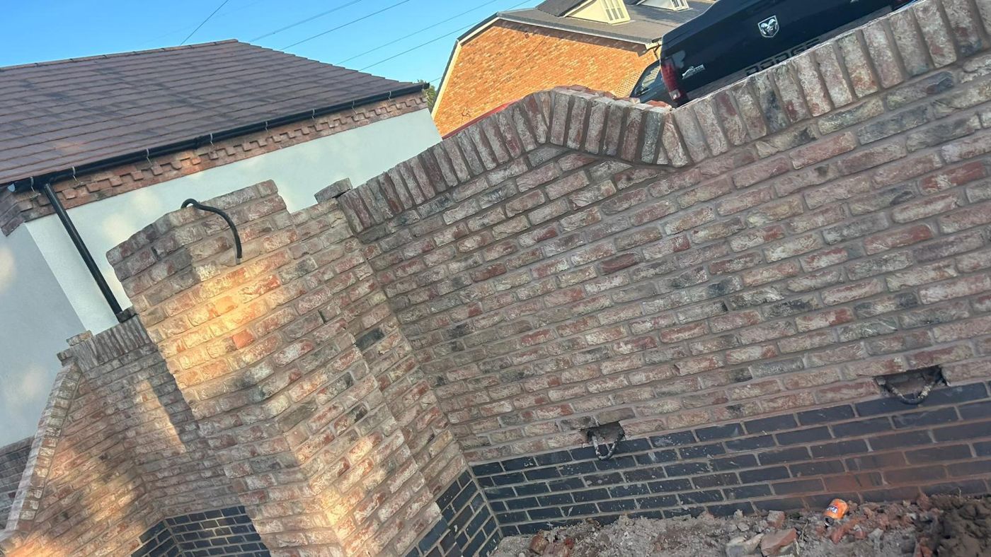 Reclaimed brick boundary wall with a raked section, piers and soldier course coping