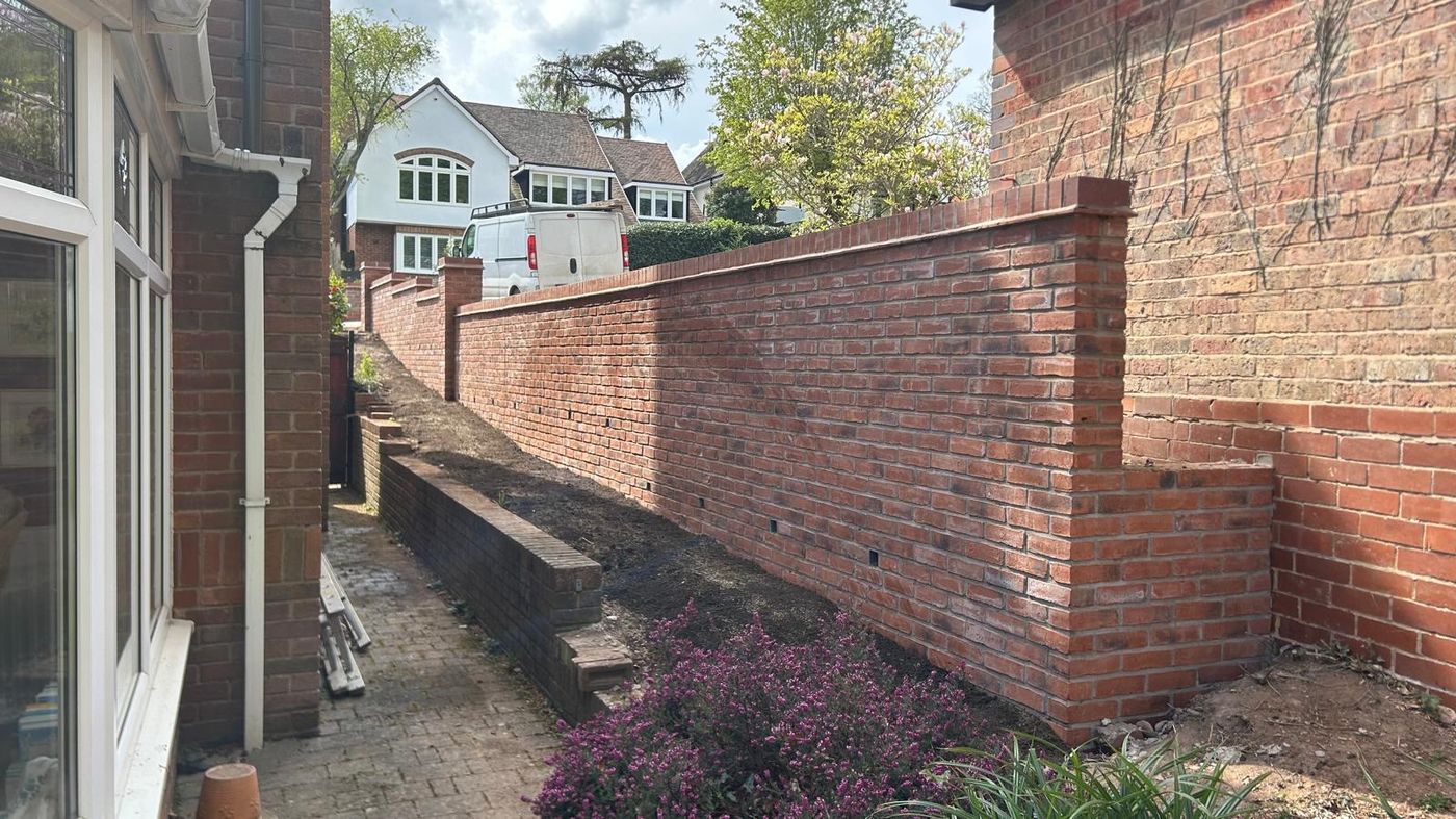 Long red brick retaining wall stepping up a sloped garden