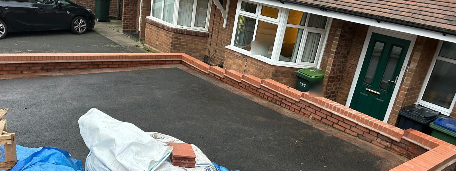 New tarmac driveway enclosed by low red brick walls
